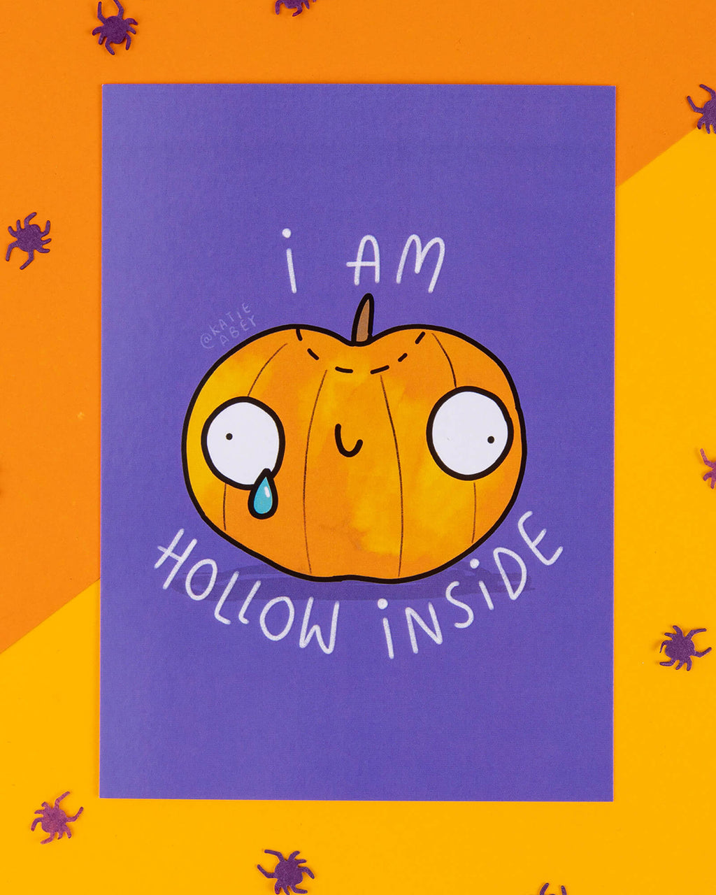 A Halloween-themed A6 postcard featuring a cartoon pumpkin with wide eyes and a single tear, with the phrase “I Am Hollow Inside” on a purple background. Designed by Katie Abey, this cheeky and relatable card is ideal for alternative millennials who love spooky humour, quirky stationery, and weirdly wonderful seasonal gifts.