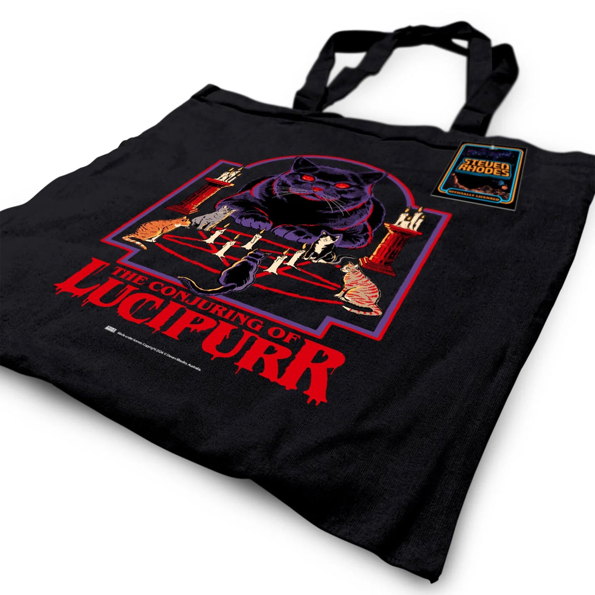 A black tote bag featuring Steven Rhodes’ “The Conjuring of Lucipurr” design. The artwork shows a black cat with glowing red eyes sitting amidst candles and a pentagram, exuding gothic and occult vibes. The text “The Conjuring of Lucipurr” appears in bold red, dripping letters. A perfect blend of spooky and quirky style.