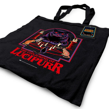 A black tote bag featuring Steven Rhodes’ “The Conjuring of Lucipurr” design. The artwork shows a black cat with glowing red eyes sitting amidst candles and a pentagram, exuding gothic and occult vibes. The text “The Conjuring of Lucipurr” appears in bold red, dripping letters. A perfect blend of spooky and quirky style.