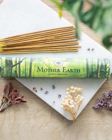 A pack of Green Tree Mother Earth Masala Incense Sticks with a nature-inspired green box design featuring forest imagery. Includes 12 hand-rolled incense sticks, perfect for creating a grounding and calming atmosphere during yoga, meditation, or rituals. Surrounded by dried flowers on a wooden surface.