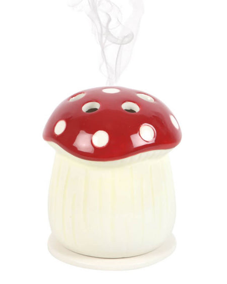 A ceramic incense cone holder shaped like a red mushroom with white polka dots, emitting a gentle trail of smoke from the top.