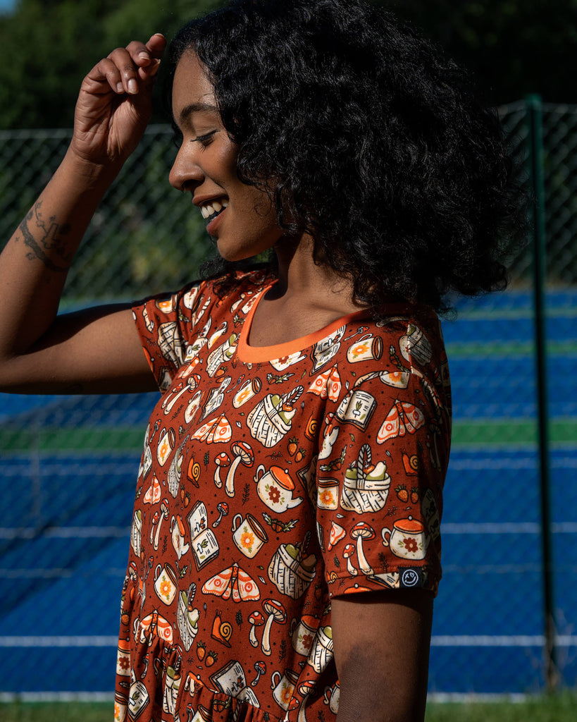 Close-up of the Mushroom Tea Party Midi Dress material, showing illustrated woodland motifs including mushrooms, moths, baskets, snails, and teapots.