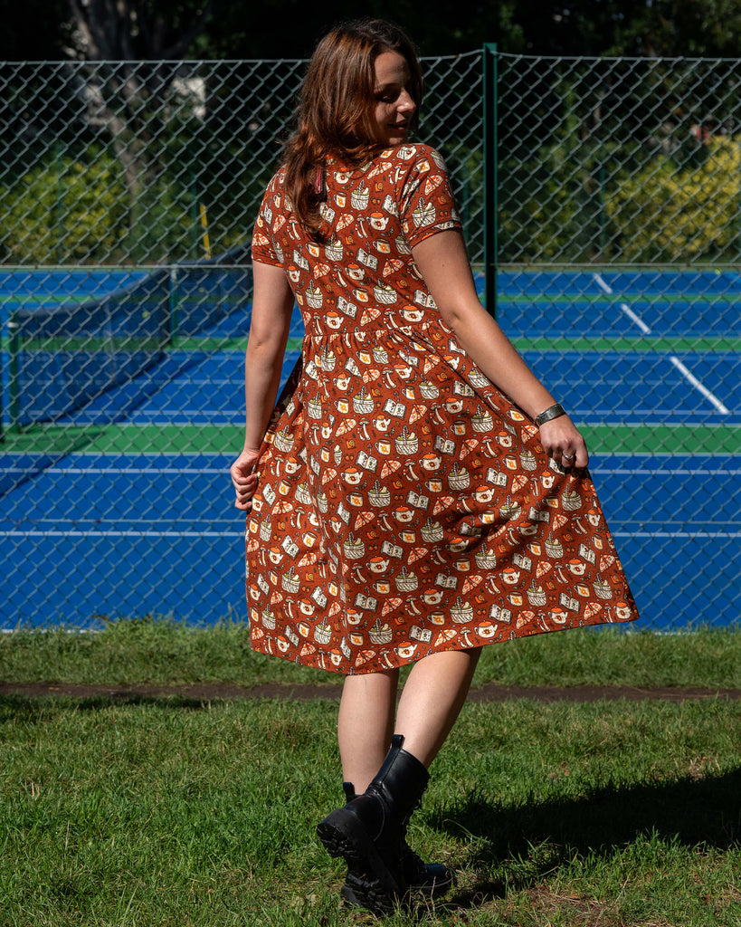 Back view of the Rebel Romance Mushroom Tea Party Midi Dress, showing the rust-orange woodland print with mushrooms, moths, and teapots, styled with black sandals.