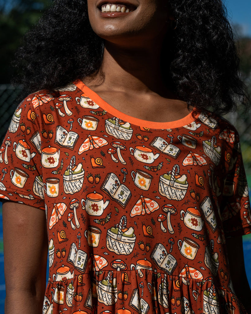 Close-up of the Mushroom Tea Party Midi Dress material, showing illustrated woodland motifs including mushrooms, moths, baskets, snails, and teapots.