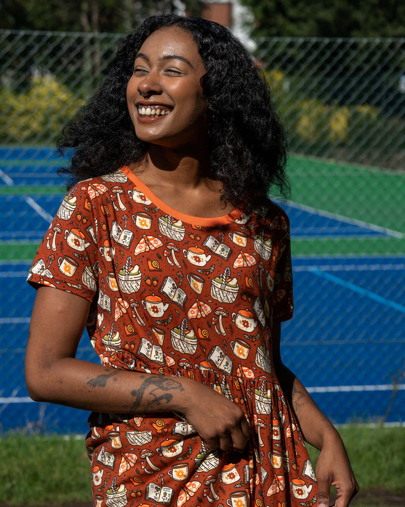 Close-up of the Mushroom Tea Party Midi Dress material, showing illustrated woodland motifs including mushrooms, moths, baskets, snails, and teapots.