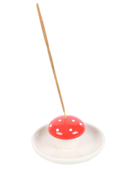 Mushroom incense holder placed on a white surface with green leaves in the background.