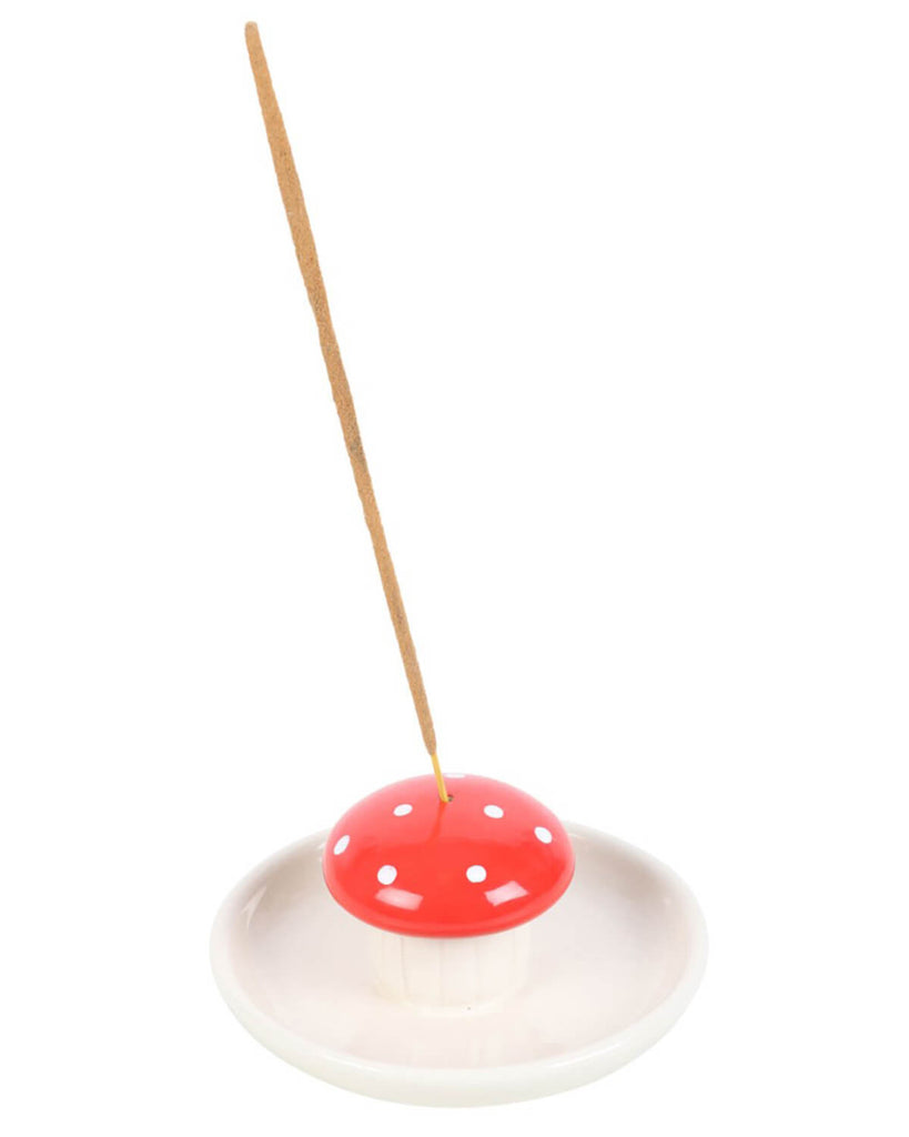 Mushroom incense holder placed on a white surface with green leaves in the background.
