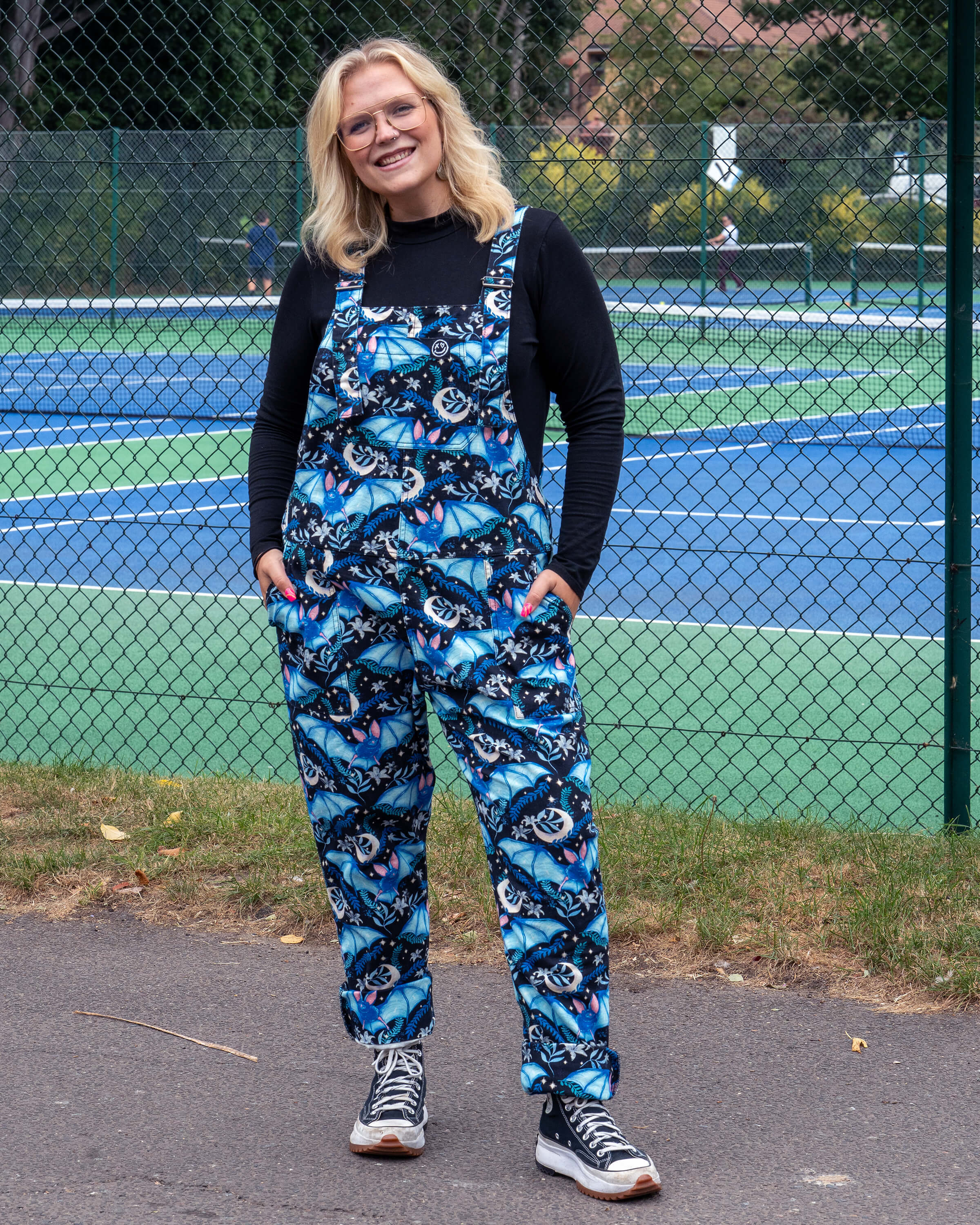 Betty wears Rebel Romance Night Flight Stretch Dungarees with a bold blue bat print, styled over a black top. The ethical slow fashion design is relaxed, comfy and alternative, perfect for millennial style lovers.