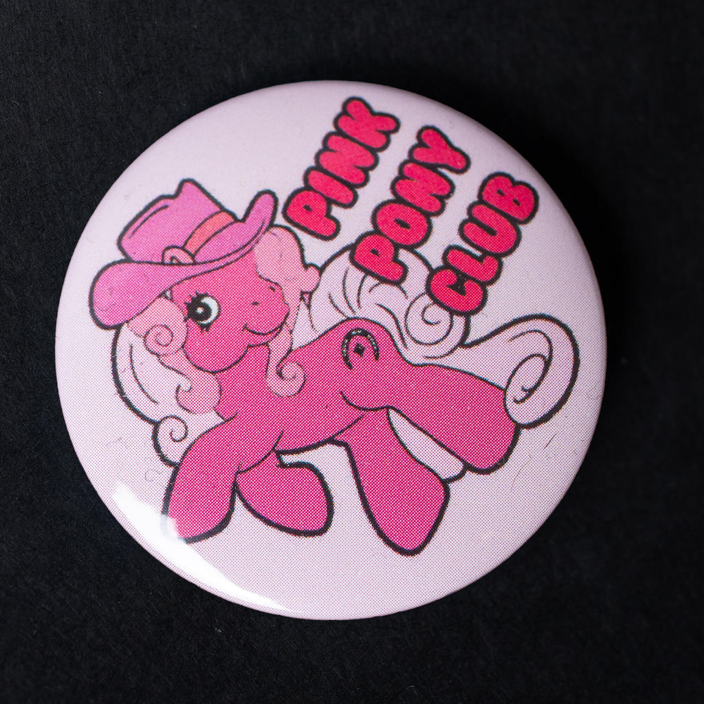 A high-gloss 38mm button pin badge featuring a pink pony with a cowboy hat and curly mane, alongside the text “Pink Pony Club” in bold red lettering. A fun pop culture-inspired accessory designed by Bite Your Granny.