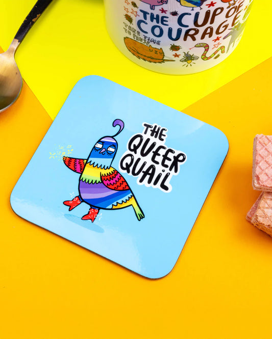 Rebel Romance’s The Queer Quail coaster, designed by Katie Abey, displayed on a bold yellow backdrop with a spoon, mug and wafers. Featuring a rainbow‑striped quail in red boots, this fun, vibrant coaster is perfect for alternative, millennial‑friendly homeware.