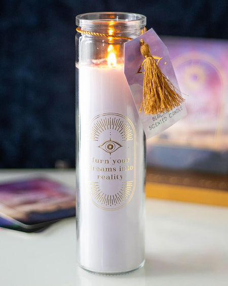 A tall blackberry-scented tube candle with a gold “Turn your dreams into reality” design, tied with a gold tassel and purple tag. Amethyst crystal chips are visible on the candle’s surface.