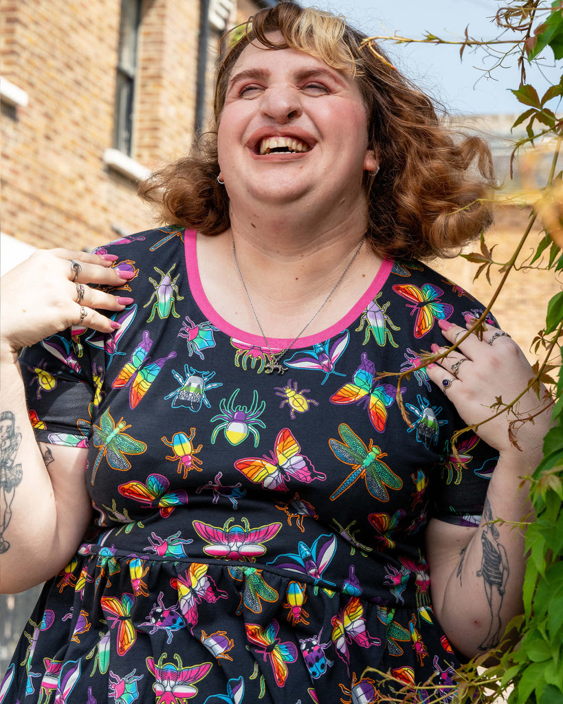 Close‑up of Maddie laughing while modelling the Rebel Romance OUTLET PRIDE Bugs Stretch Smock Dress. The colourful rainbow insect print and pink trim stand out, celebrating quirky slow fashion from this unique UK brand.