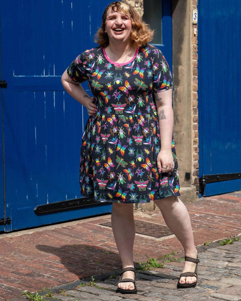 Maddie laughs in the sun, modelling the Rebel Romance OUTLET PRIDE Bugs Stretch Smock Dress. The rainbow insect print and comfy smock style make this ethical UK dress a vibrant alternative statement.