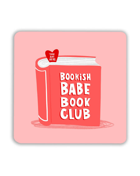 Square pink coaster featuring a red illustrated book with bold white text that reads “Bookish Babe Book Club.” A small red heart-shaped bookmark at the top says “You Are Here.”