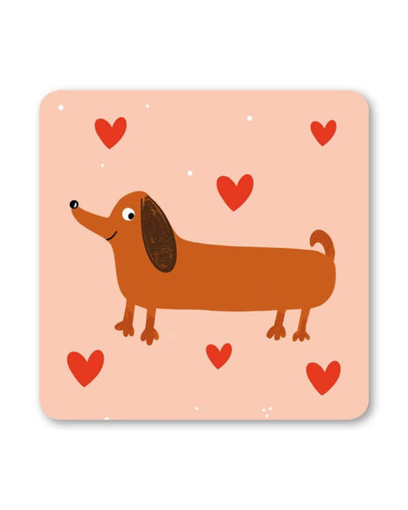 Square peach-coloured coaster featuring a brown sausage dog with a happy expression, surrounded by scattered red hearts and tiny white dots.