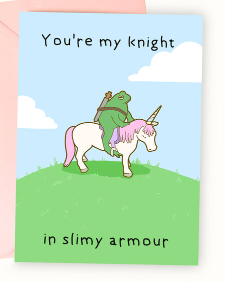 A greeting card featuring a whimsical illustration by Nimbob of a heroic green frog dressed as a knight, riding a white unicorn with pink hair and a golden horn. The frog carries a sword on its back and looks determined. The background is a bright blue sky with fluffy white clouds, and the text above reads ‘You’re my knight’ while the text below reads ‘in slimy armour’ in a playful handwritten font. A fun and charming card, perfect for friendships, anniversaries, or just to make someone smile!