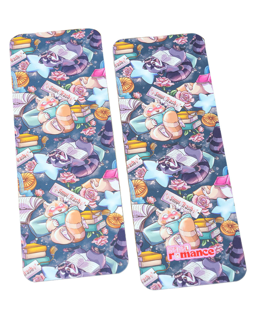  A pair of glossy rectangular bookmarks featuring a repeated “Smut Trash” pattern with raccoons and red pandas reading books, surrounded by books, flowers, and snacks. Designed by Rebel Romance.