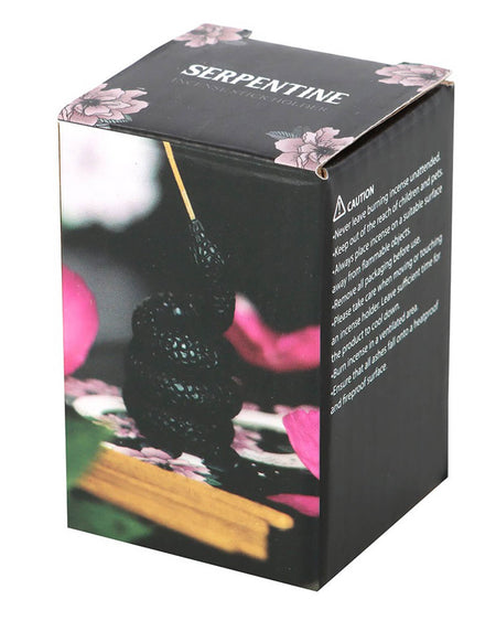  A black box with pink floral accents showing a coiled black snake incense holder with an incense stick. The box displays the product name “Serpentine Incense Stick Holder” and safety instructions on the side.