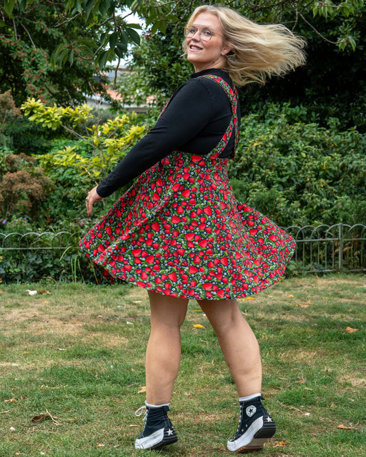 Model Betty twirls in the Rebel Romance Strawberry Field Flared Pinafore, showing the flared skirt detail against a garden backdrop.