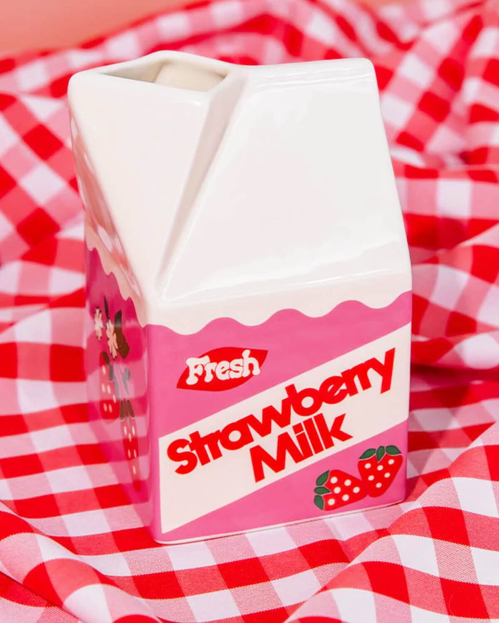 Close-up of a ceramic strawberry milk vase with a retro design, featuring a pink and white milk carton shape with “Fresh Strawberry Milk” text and cute strawberry illustrations. Perfect for flowers, stationery, or decor.