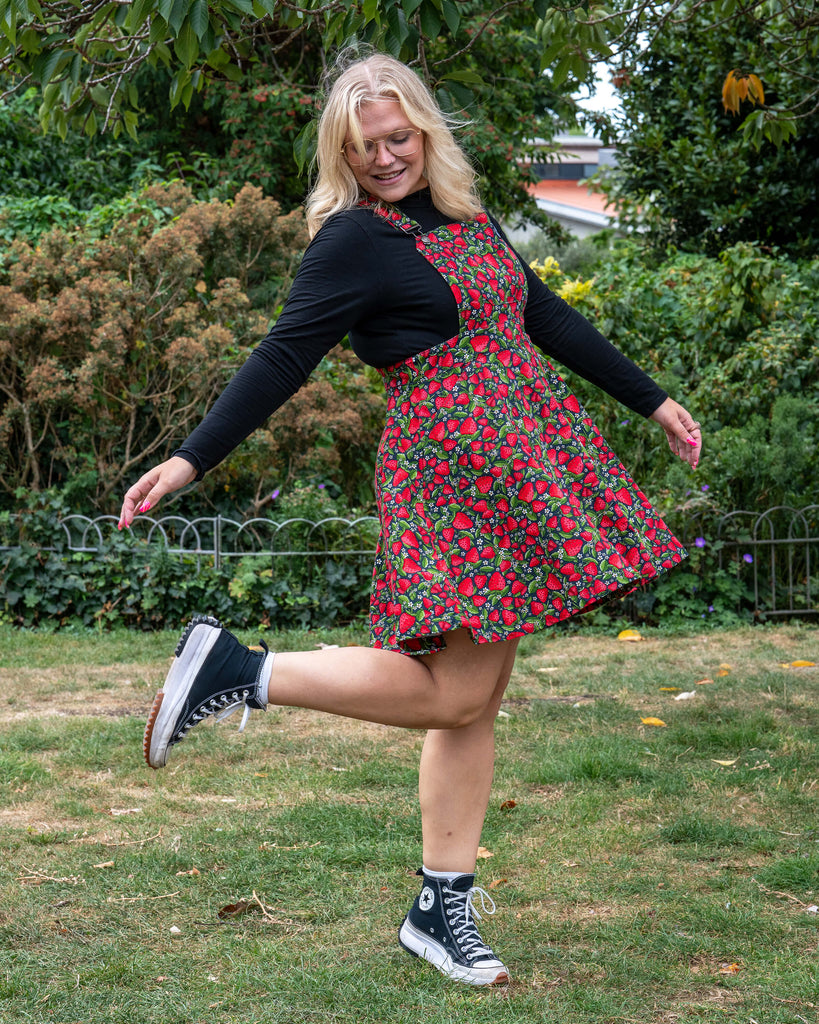 Model Betty twirls in the Rebel Romance Strawberry Field Flared Pinafore, showing the flared skirt detail against a garden backdrop.