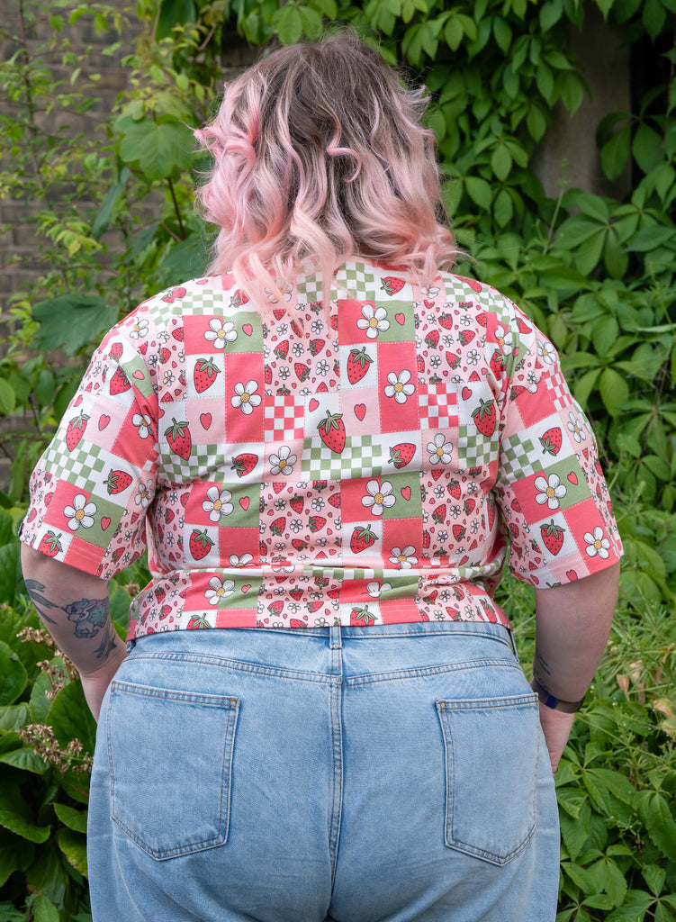 Back view of Sam wearing the Strawberry Picnic tee, showing how the print continues across the back and sleeves.
