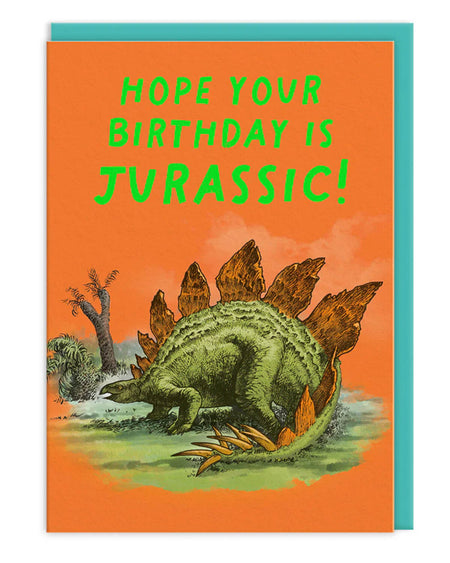 Stegosaurus birthday card with neon green text reading “Hope Your Birthday Is Jurassic!” on an orange background, featuring a detailed illustration of a stegosaurus and paired with a bright teal envelope.