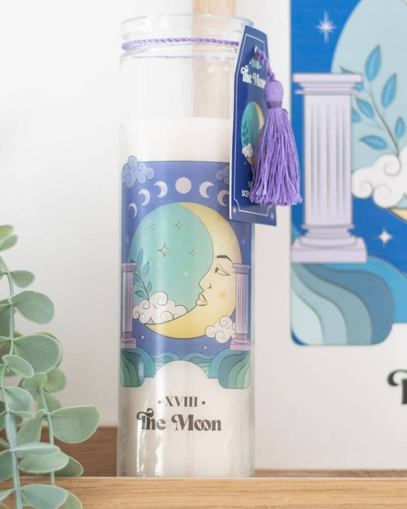 The Moon Violet Tube Candle styled on a wooden shelf with eucalyptus leaves in the background.