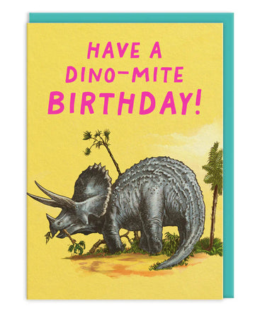 Triceratops birthday card with a vintage-style dinosaur illustration on a bright yellow background and bold pink text that says “Have a Dino-Mite Birthday!” paired with a turquoise envelope.