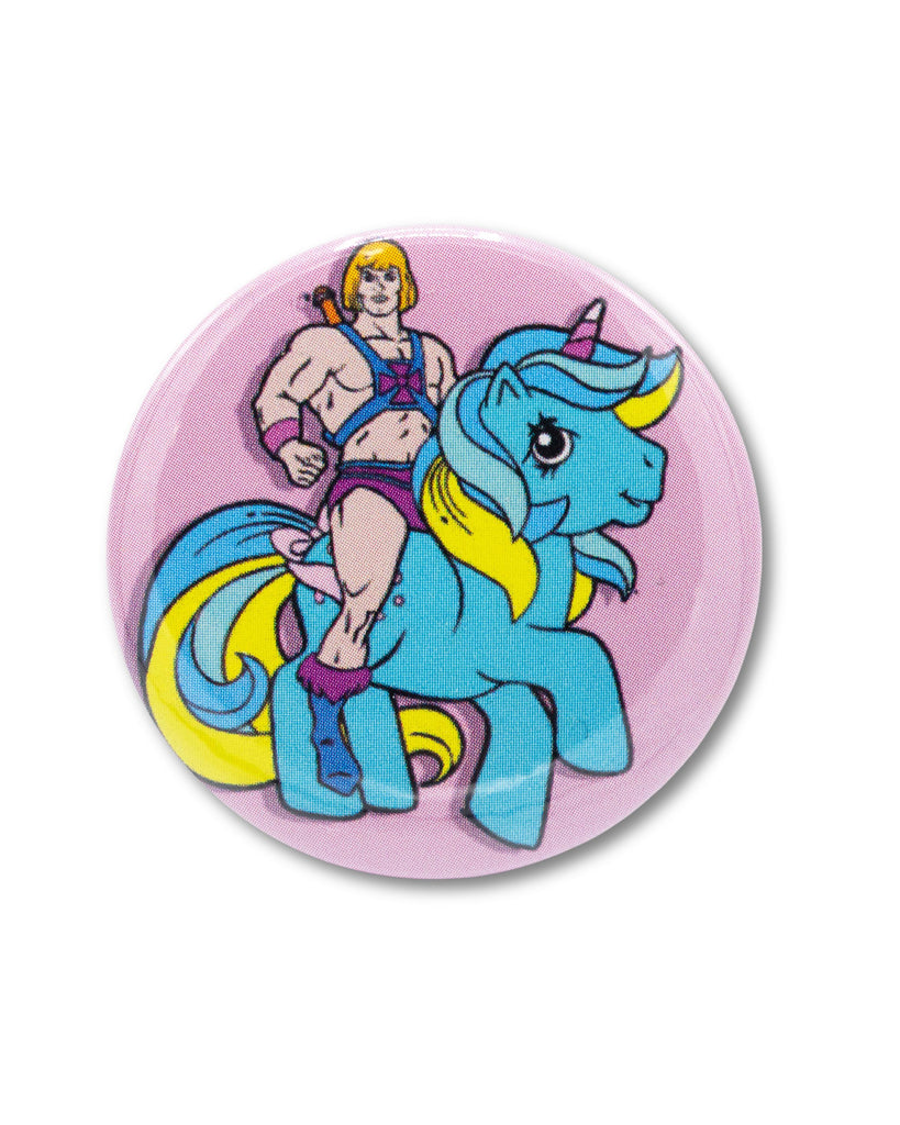 Pink button badge with a cartoon character, he man, riding a blue my little pony unicorn. A retro 80s design from Bite Your Granny.