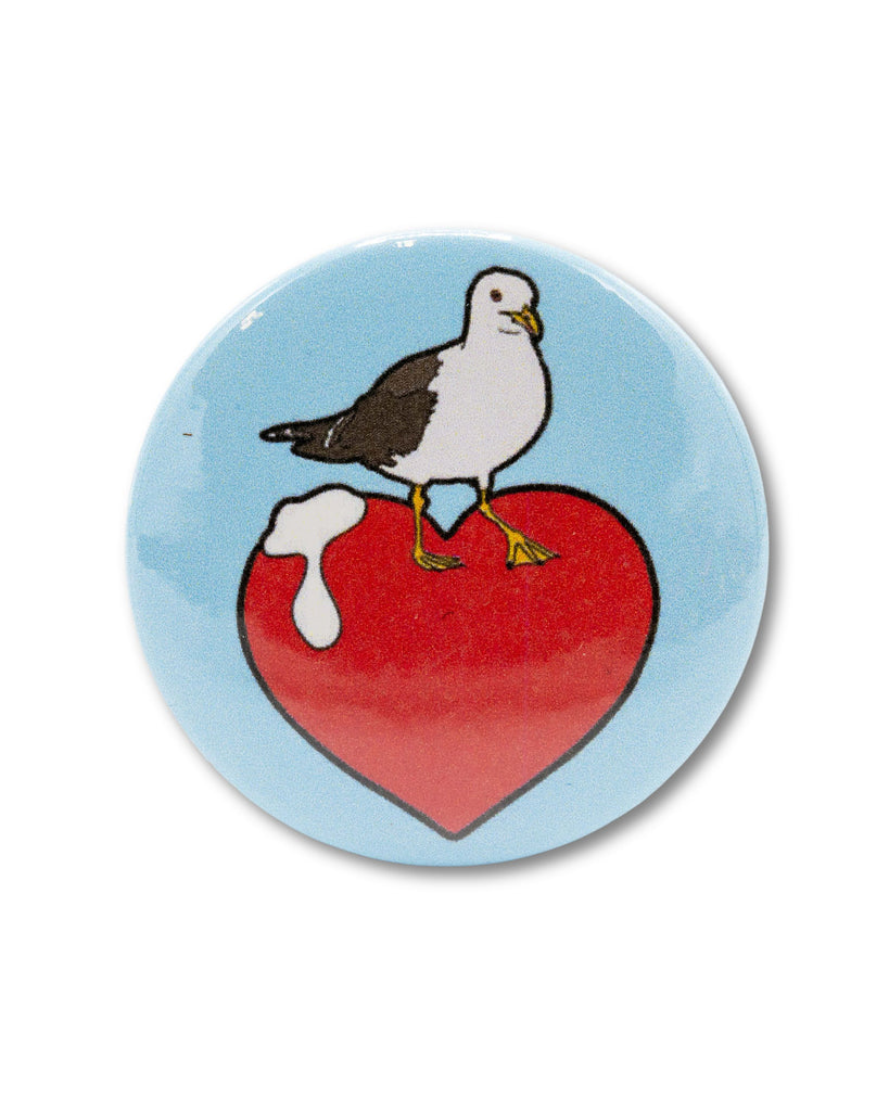 Blue button badge with a seagull doing a poo on a red heart. A silly retro inspired design from Bite Your Granny.