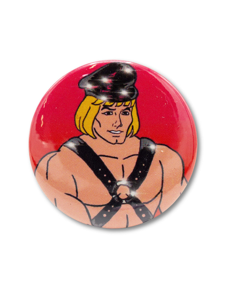 Red button badge with a cartoon character, he man, wearing a fetish outfit with sparkles. An 80s retro design from Bite Your Granny.