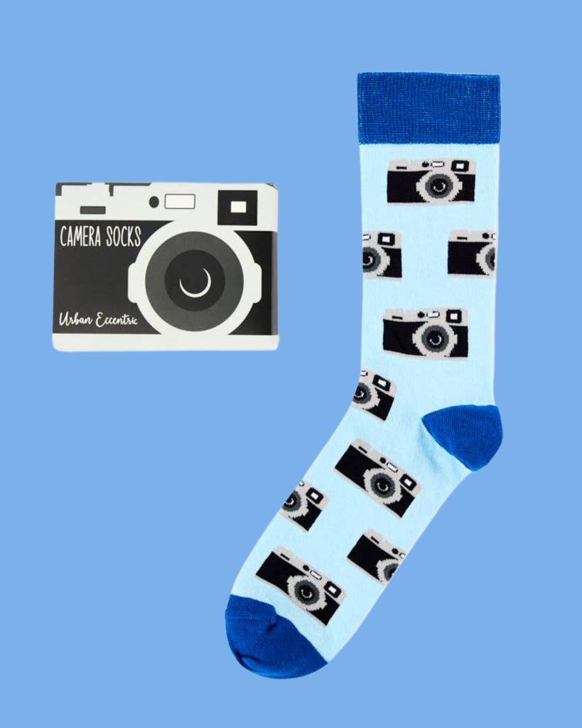 Urban Eccentric camera socks with vintage camera design on pale blue background, shown alongside novelty camera-shaped packaging. Available at Rebel Romance.