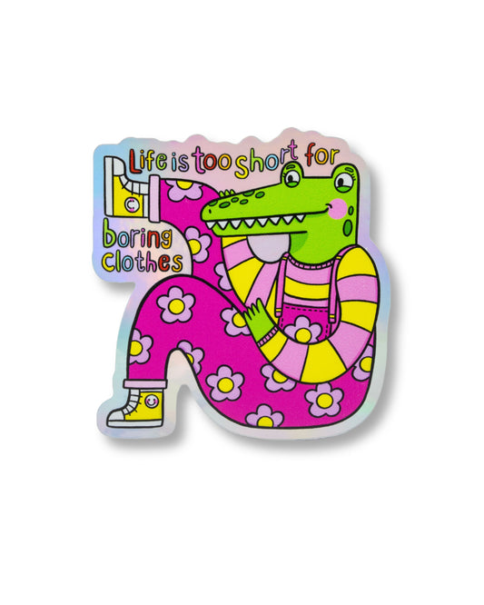 Holographic vinyl sticker from Rebel Romance featuring a bright green crocodile in dopamine-dressing floral overalls with the slogan “Life is too short for boring clothes.” Designed by Kellylou, this waterproof matte sticker celebrates quirky, bold fashion and alternative style. Perfect for customising laptops, notebooks, or mirrors. Ideal for fashion lovers and sticker collectors.