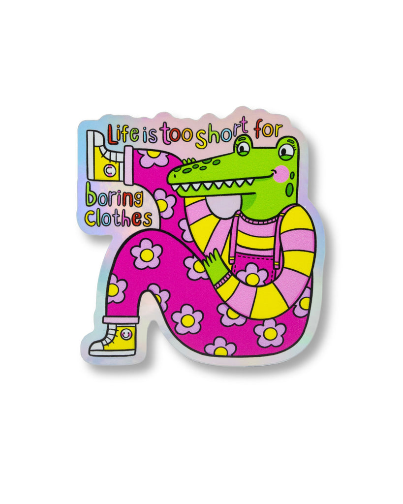 Holographic vinyl sticker from Rebel Romance featuring a bright green crocodile in dopamine-dressing floral overalls with the slogan “Life is too short for boring clothes.” Designed by Kellylou, this waterproof matte sticker celebrates quirky, bold fashion and alternative style. Perfect for customising laptops, notebooks, or mirrors. Ideal for fashion lovers and sticker collectors.