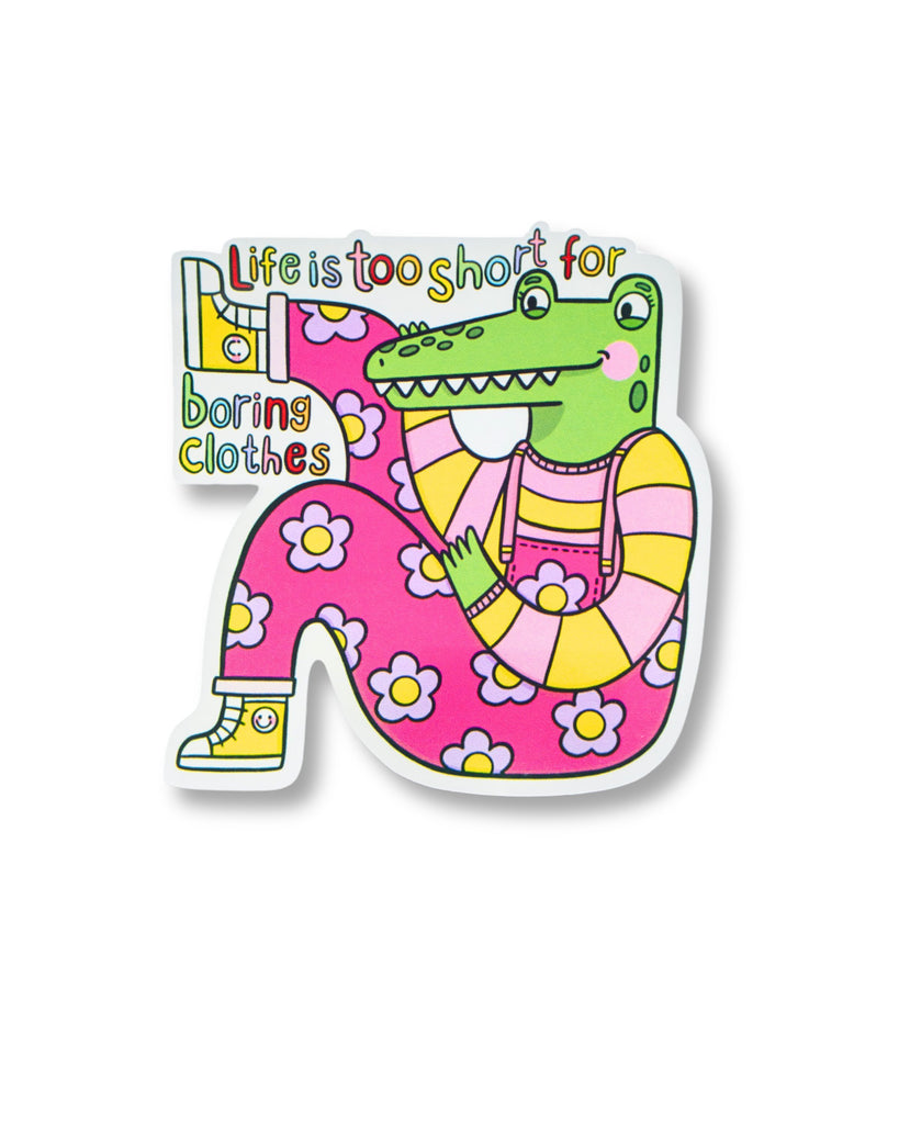 Glossy vinyl sticker from Rebel Romance featuring a green cartoon crocodile in a pink daisy-print outfit with striped sleeves, holding up a yellow boot. Surrounded by colourful text that reads “Life is too short for boring clothes.” Illustrated by Kellylou, this dopamine-dressing inspired sticker celebrates quirky, fun, alternative fashion. A bold, joyful accessory from a small UK business known for embracing the extraordinary.