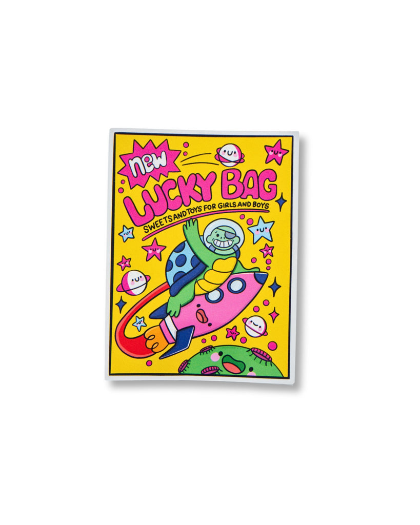 Glossy 90s-style sticker illustrated by Kellylou, sold by Rebel Romance, a UK brand celebrating alternative fashion and nostalgic aesthetics. The colourful sticker features a smiling monkey astronaut riding a pink rocket through space, surrounded by planets, stars, and kawaii smiley faces on a bright yellow background. Bold pink lettering reads “Lucky Bag – Sweets and Toys for Girls and Boys”.