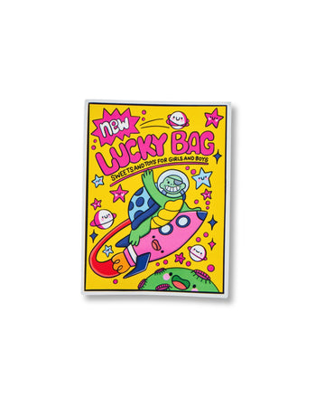 Glossy 90s-style sticker illustrated by Kellylou, sold by Rebel Romance, a UK brand celebrating alternative fashion and nostalgic aesthetics. The colourful sticker features a smiling monkey astronaut riding a pink rocket through space, surrounded by planets, stars, and kawaii smiley faces on a bright yellow background. Bold pink lettering reads “Lucky Bag – Sweets and Toys for Girls and Boys”.