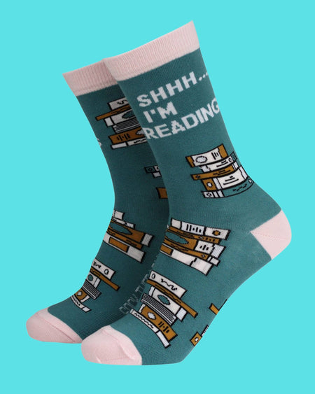 Smiling Faces bamboo socks in teal with charming illustrations of stacked books and the phrase 'Shhh… I'm Reading'. Sustainable socks with pastel pink details, ideal gift for readers from Rebel Romance.