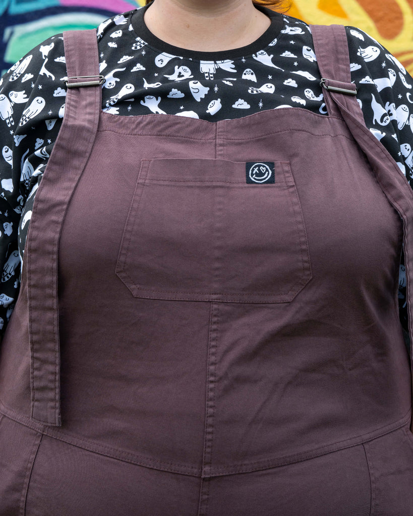 Close-up of the bib section of the Plum Mocha dungarees, showing the chest pocket and Rebel Romance logo patch.