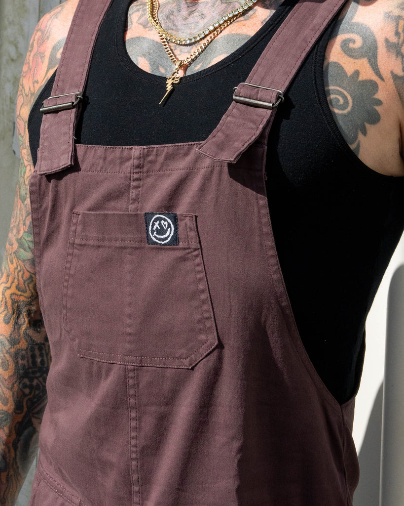 Close-up portrait of James smiling in the Plum Mocha dungarees with the bib and pocket detail visible.