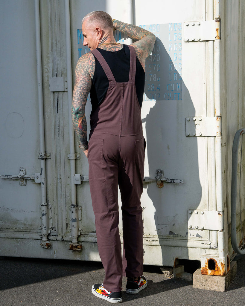 Back view of James wearing the Plum Mocha dungarees, hand on head, showing slim leg fit.