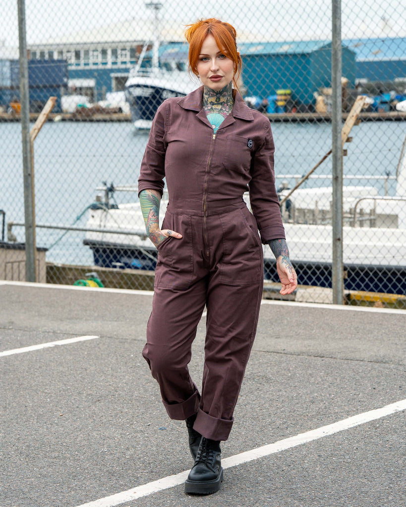 Erin models the Plum Mocha Boiler Suit by Rebel Romance, a utility-style jumpsuit with a zip fastening, collar and pockets. Styled with rolled-up hems and chunky black boots, photographed outdoors by the harbour for an edgy streetwear vibe.