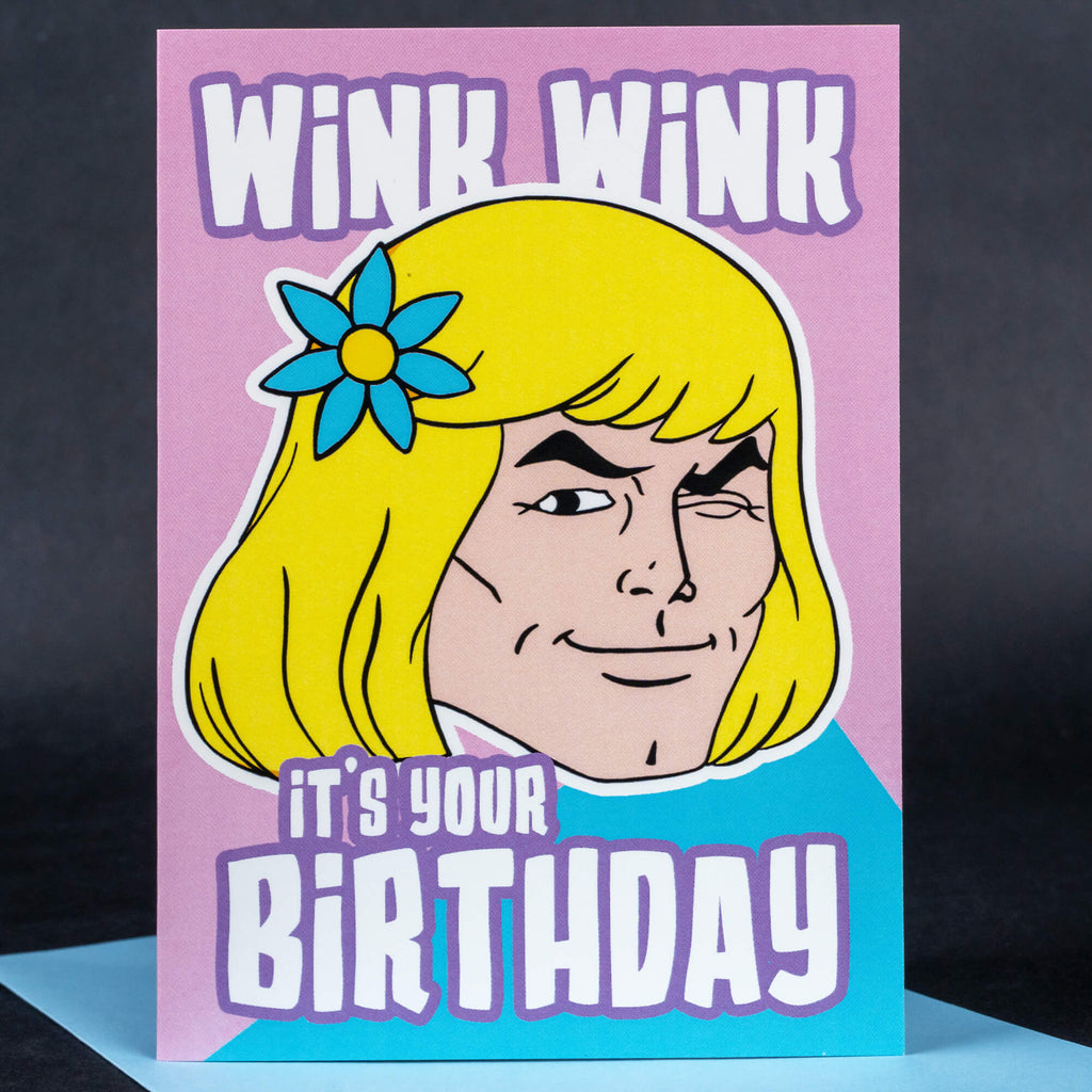Humorous birthday card with a retro-style illustration of a winking man in blonde hair and a flower accessory, accompanied by the text ‘WINK WINK, it’s your BIRTHDAY’ in bold pastel colours.