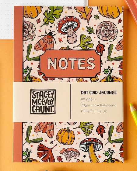 A close-up of the notebook front cover with the word “NOTES” framed in orange. The cream band displays details: “Dot Grid Journal, 80 pages, 90gsm recycled paper, Printed in the UK.”
