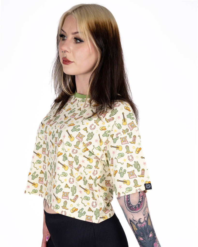 Model Florence (@florencerosaria) wears the Rebel Romance x Yasmin Cousins Cowboy Cropped Boxy Tee in size 10. The cream tee with a Western-inspired print is paired with black trousers. Florence is a UK size 8/10 and 5'3". Rebel Romance is a small UK business celebrating bold style and inclusive fashion for millennials.