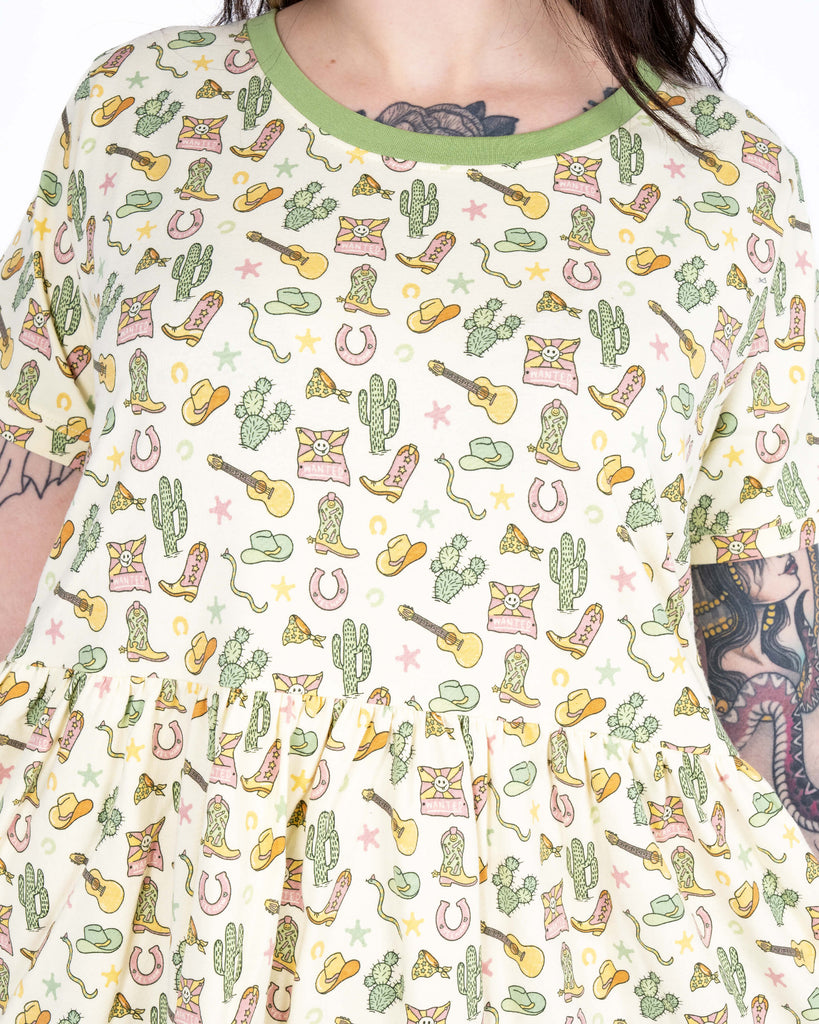 Detailed view of the upper bodice of the cream smock dress, showing colourful cowboy-themed illustrations and light green neck trim.