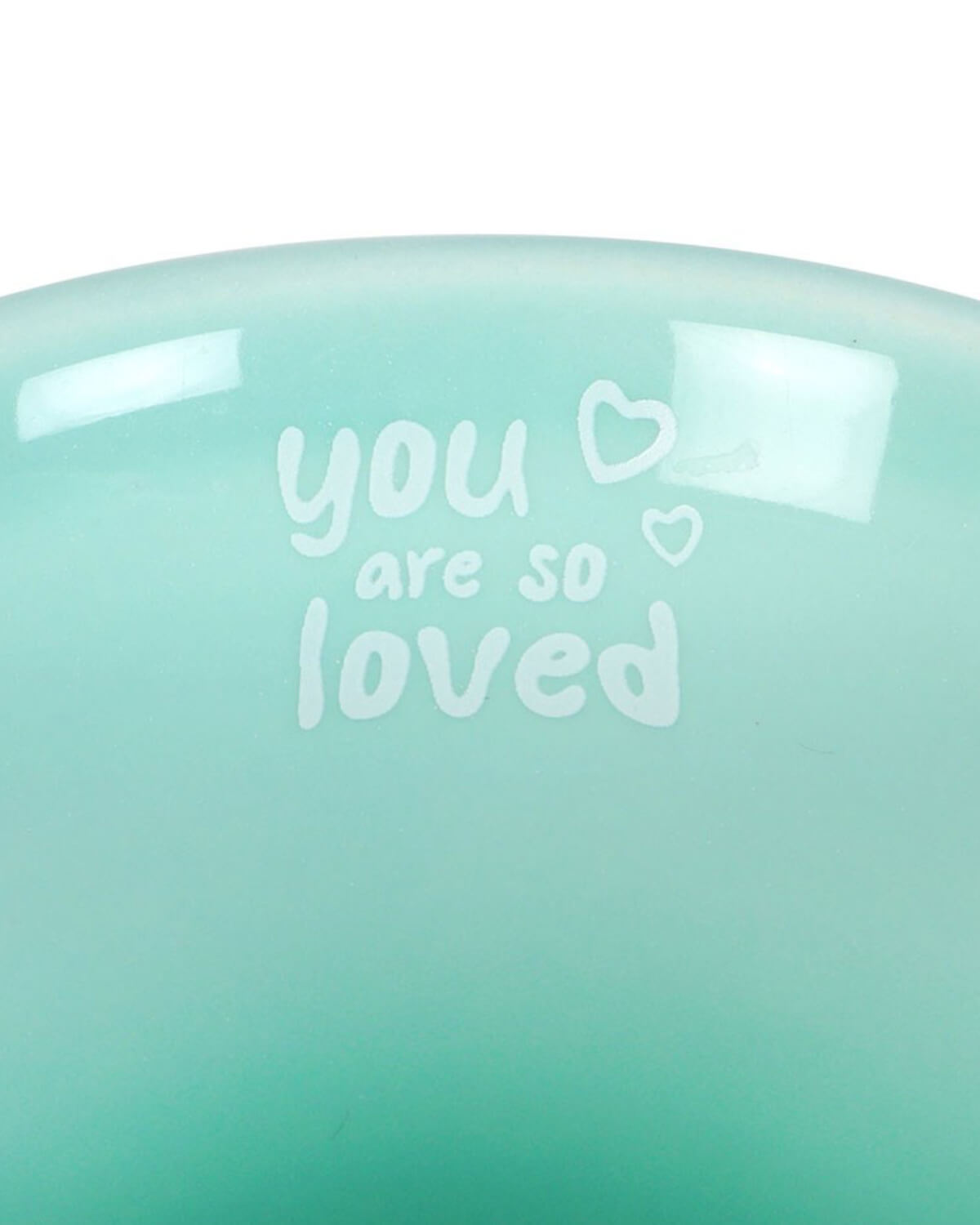 Close-up of a mint green ceramic mug with a blue happy face design and ‘You Are So Loved’ text on the inner rim.