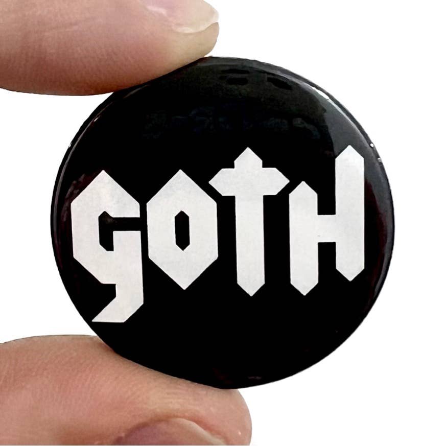 A high-gloss 38mm pin badge with bold white “GOTH” text in gothic-style font on a sleek black background. Held between fingers, the badge gleams under the light, highlighting its smooth finish.