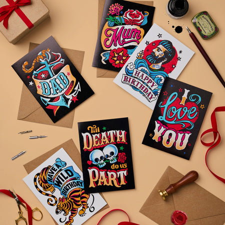 A mix of tattoo-inspired greeting cards, including “Til Death Do Us Part,” “Love You,” “Happy Birthday,” and more, paired with recycled craft envelopes. Designs feature vibrant colours, vintage typography, and striking foil finishes.